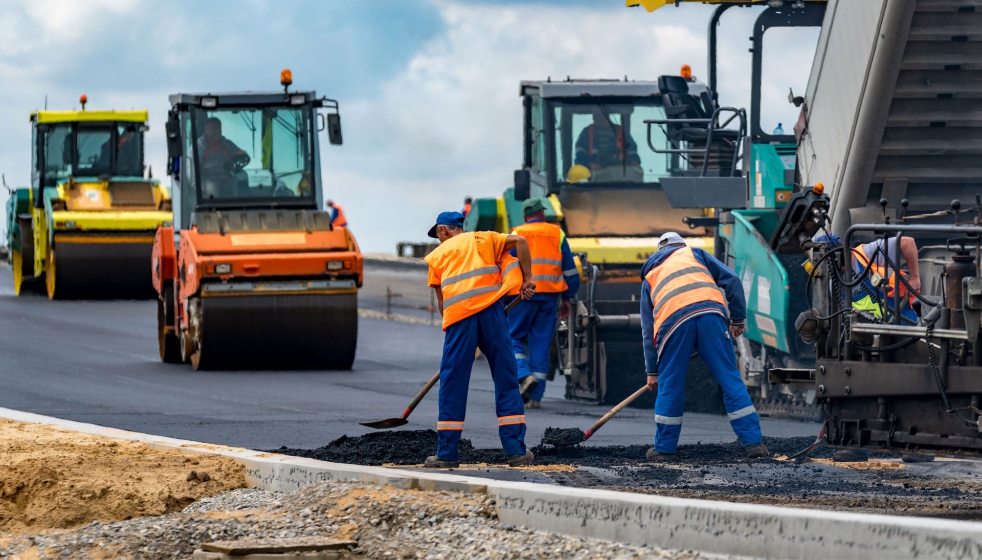 A group of construction workers wearing hard hats and reflective vests, operating heavy machinery and laying down asphalt on a newly excavated road in Sacramento, showcasing the intricate process of building a sturdy and smooth surface.